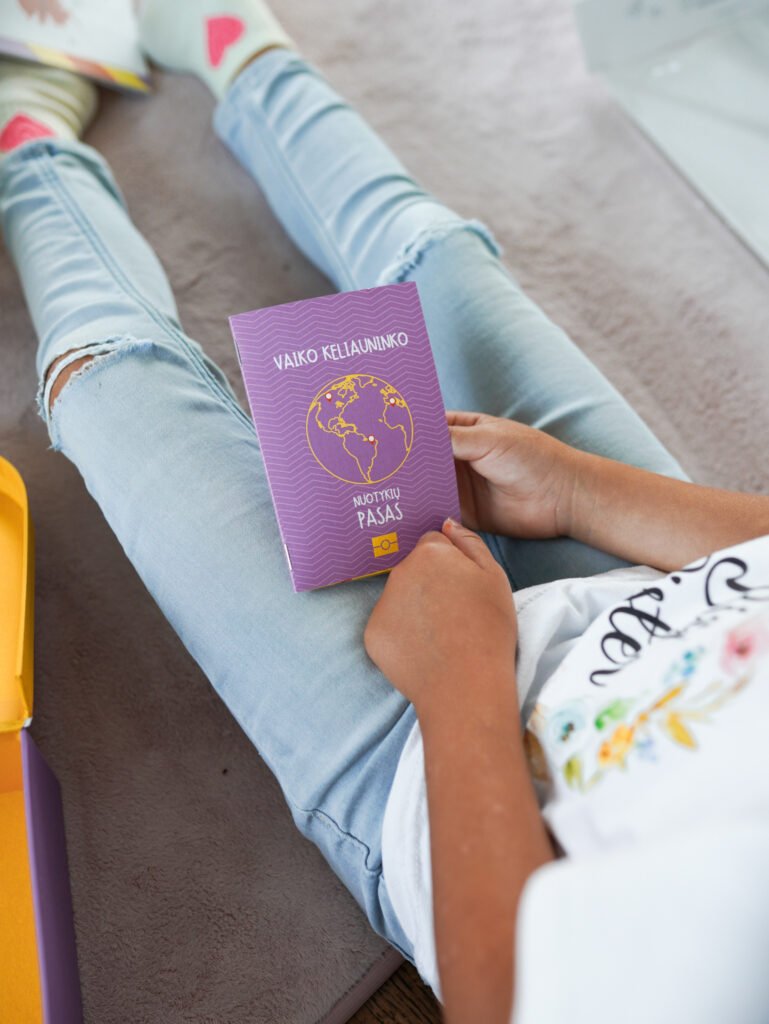 Person seated on a rug holds a purple passport-style booklet with a globe illustration on the cover while wearing ripped light-blue jeans.