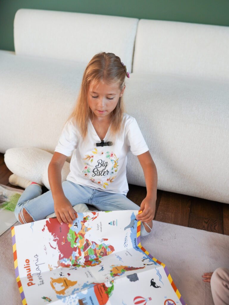 Young girl sitting on the floor, looking at a colorful world map book.