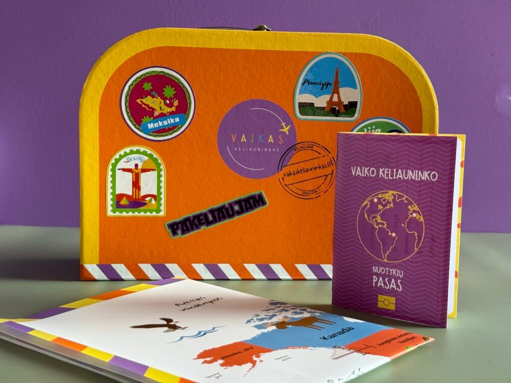 Bright orange suitcase covered in colorful travel stickers sits beside a purple notebook and printed maps on a desk against a purple wall.