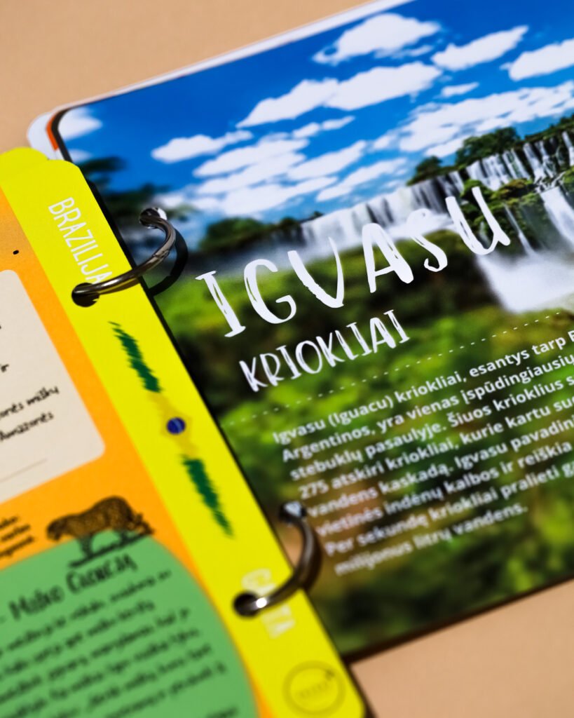 Close-up of a glossy travel brochure held in a bright yellow binder, showing a blue sky with white clouds and bold white text partially visible at the edge grip ring near the binder.