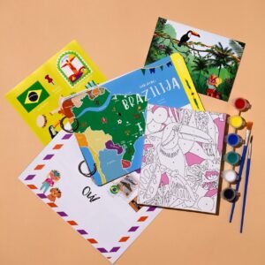 Flat lay of colorful travel books, a Brazil map, a coloring page, and watercolor paints with brushes on a peach background.