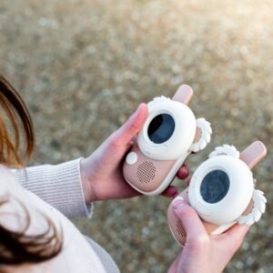 Two pink and white children's toy devices with round screens and wing-like decorations held in both hands.
