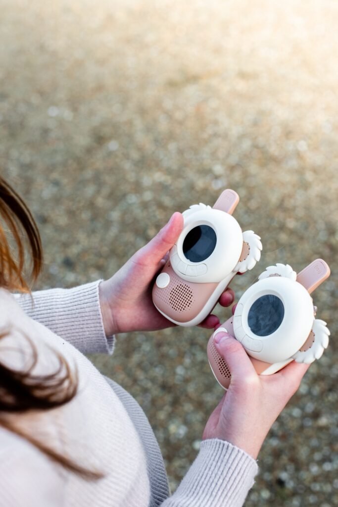 Two pink and white children's toy devices with round screens and wing-like decorations held in both hands.