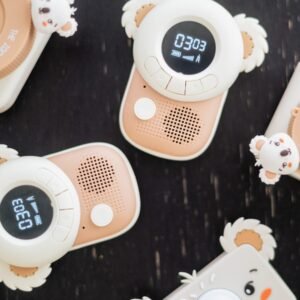 Pastel pink and white children's toy cameras with fluffy koala-ear accents on a dark surface.