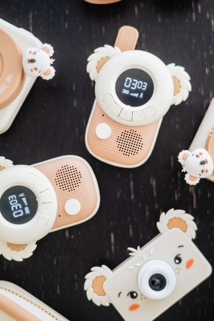 Pastel pink and white children's toy cameras with fluffy koala-ear accents on a dark surface.