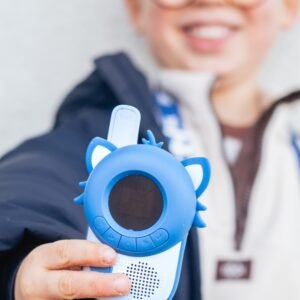 A child wearing glasses holding up a blue handheld kids' toy with a round display and cat-ear accents toward the camera.